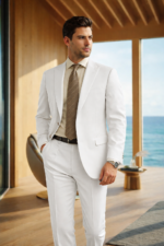 Male model wearing an off-white slim fit two-piece suit with beige tie, standing in a modern seaside interior setting.