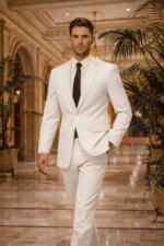 Man wearing a white suit with black tie walking in a luxurious hotel lobby.