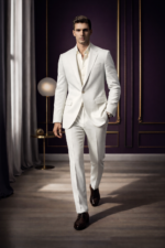 Male model walking confidently in a white slim fit two-piece suit with open collar shirt in an elegant indoor setting