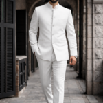 Man wearing a white bandhgala suit walking in a stone corridor.