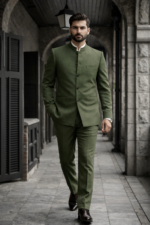 Man wearing an olive green bandhgala suit walking in a stone corridor.
