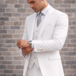 Man wearing a white three-piece suit adjusting his cuff against a brick wall background.