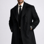 Man wearing a black double-breasted overcoat over a formal suit and tie, showcasing premium men's tailored outerwear.